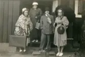 Fotografi från 1945 taget i Vislanda, senare del av Alvesta kommun i Småland. Tre kvinnor bär ytterkläder, varav den fjärde bär en dubbelknäppt herrkostym, skjorta, slips, hatt och har en pipa i munnen.
