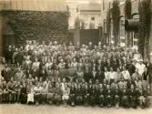 Fotografi från 1930 som visar personalstyrkan uppradad framför sin arbetsplats på Göteborgs Gardinfabrik AB, som då ligger vid Getebergsäng. Vi ser att här samsas både fabriksarbeterskor, fabriksarbetare, maskinister och övrig personal som arbetar nere på golvet, med förmän och andra högre upp i rang.
Det går bland annat att se en man som bär dubbelknäppt uniform och tillhörande uniformsmössa och snett till vänster bakom honom skymtar en till man iklädd samma mundering. De ser ut att vara chaufförer eller portvakter. 

Arbetsstyrkan har ställt upp sig på innergården till fabriken och det går tydligt att urskilja gatstenen som marken är belagd med samt murgrönan som växer utanpå fasaderna. 