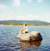 Fotografi som visar Inga-Lill Börjesson sittande ovanpå en sten ute i vattnet och blicka ut över den solbelysta vattenytan. Enligt en notering i fotoalbumet står dessutom: 