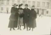 Tre kvinnor och en herre på stortorget, Växjö, en vintrig dag i januari 1922. 
Fr.v.: fröken Gertrud Eksandh, fru Gurli Eksandh, Yngve Eksandh och fru Elsa Laudien (f. Eksandh). I bakgrunden syns residenset.	
Enl. text på baksidan: 