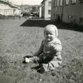 Porträtt av Lennart Berndtsson som sitter i gräset mellan husen i ett bostadsområde. Prytzgatan i Broslätt, Mölndal, år 1954.