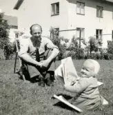 Pojken Lennart Berndtsson sitter i gräset mellan husen i ett bostadsområde tillsammans med sin farfar Bertil 