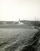 Bilden visar ett öppet landskap med Växbo kapell i bakgrunden som hör till Bollnäs församling.