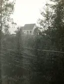 Byggnad som är under uppbyggnad i bakgrunden samt med skog och gärdsgård i framgrunden av fotografiet.