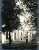 Exteriören av Heliga Trefaldighetskyrkan i Gävle med träd i förgrunden.