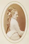 En ung kvinna i ljus klänning med ryschkrage. Man anar ett mörkt sammetsband runt halsen.
Midjebild, halvprofil. Ateljéfoto.
Fru Mathilda Aminoff, f. Lindström (1854-1943), från Kronobergs kungsgård, Växjö.