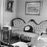 Stoppad soffa med minre sybord framför. Ovanför soffan hänger två målningar. Interiörbild från Torborg Lindéns hem på Södra Ringgatan 12, kv Trädgården, Alingsås. Bilden tagen av hennes son Erik Lindén 1949.