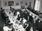 50-årsjubileum den 3 juli 1954 för Kustsanatoriet Apelviken. Middag vid långbord på Societetsrestaurangen. Gästerna tar mat från serveringspersonalen stora brickor. Längs väggarna står skärmar med modern konst. (Se bildnr KSA137-KSA159.)