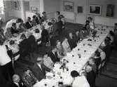50-årsjubileum den 3 juli 1954 för Kustsanatoriet Apelviken. Middag vid långbordd på Societetsrestaurangen. En gäst tar från servitörens serveringsfat. Längs väggarna står skärmar med modern konst.
