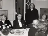 50-årsjubileum den 3 juli 1954 för Kustsanatoriet Apelviken. Troligen är det borgmästare Axel Lindskog som står och håller ett tal vid middagen på Societetsrestaurangen. Han blev ledamot i direktionen för Kustsanatoriet 1961-1976. På bordet står en skål med nejlikor, ett askfat och vid den ligger en tidning. (Se bildnr KSA137-KSA159.)
