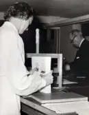 Personalens kurs i bokbinderi vid Kustsanatoriet Apelviken på 1960-talet. En kvinna håller bunten med blad till en blivande bok. I bakgrunden arbetar överläkare Albert Ahlberg med något annat moment. Bilderna har tillhört sjukhusintendent Harald Liljenberg (1908-1983). (Se bildnr KSA160-KSA169)