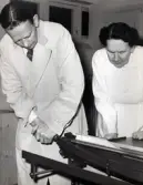 Personalens kurs i bokbinderi vid Kustsanatoriet Apelviken på 1960-talet. En man och en kvinna vid pappersskäraren. Bilderna har tillhört sjukhusintendent Harald Liljenberg (1908-1983). (Se bildnr KSA160-KSA169)