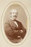 En medelålders man med mustascher, klädd i mörk kostym med stärkkrage och fluga.
Midjebild, halvprofil. Ateljéfoto.
Överste Gustaf Weidenhielm (1810-1876), Växjö.