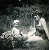 Porträtt av pojken Lennart Berndtsson och hans mor Inga Maj Berndtsson som sitter i gräset vid badplatsen 