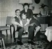 Jul på Prytzgatan 38 i Broslätt, Mölndal, cirka 1957. Porträtt av pojken Lennart Berndtsson och hans föräldrar Leif och Inga Maj Berndtsson. De sitter i en fåtölj i vardagsrummet.