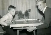 Jul, advent cirka 1959. Porträtt av två pojkar som sitter vid ett bord och spelar ett ishockeyspel. Till vänster Lennart Berndtsson och till höger Dane och Gulli Borges son Ivan.

Fotografi eventuellt taget hos paret Borge.