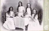 Porträtt av fyra kvinnor med långt hår och vita kläder som sitter vid ett fikabord. Text i album: 