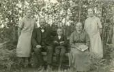 Bilden visar troligen en familj som poserar utomhus för ett fotografi, sannolikt från tidigt 1900-tal, baserat på klädstilar.