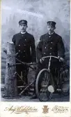 Två män i uniformsliknande kläder poserar med en tidig 