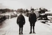 Thore Eriksson med lillebror Paul till vänster på vägen utanför sitt hem Solvik i Grimstorp, Nässjö kommun. Impregneringsstolpar till höger och samhället i fonden. Foto omkring 1930.