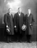 Ateljéfoto av tre unga herrar i ytterkläder med hattarna i händerna. Beställt av Rudolf Malmström, Uddeholm (Värmland).