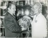 Glasdesignern Asta Strömberg, Strömbergshyttan, och en okänd man i kostym visar upp ett arbetat fat vid en glasutställning, trol. utomlands.