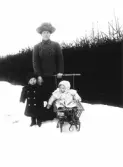En kvinna med två små barn ute i snön med en sparkkälke.