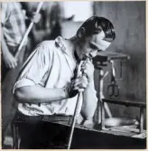 Arbete i hyttan på Strömbergshyttan. En ung man blåser i en glasblåsarpipa.
