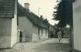Kvinna som går med ett paraply bredvid vitputsade hus med sannolikt vasstak, vilket var standard för danska gårdar på Själland, Huleröd. Danmark 1920.