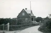 En sekelskiftesvilla med glasveranda och balkong, inramad av en uppvuxen häck samt en grind, Torekov i Skåne 1922.