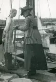 Torekov 1922. Bilden visar en kvinna och flicka som står på en kajkant vid en hamn. Kvinnan visar en nyfångad fisk för flickan.
