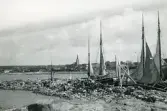 Vy över kusten i Torekov med bl a kyrka och bostäder i bakgrunden samt båtar som ligger förtöjda i förgrunden, 1922.