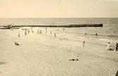 Badgäster vid strand samt en pir som går ut i havet vid Liseleje strand, Danmark 1925.