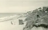 Badort med sandstrand med de ikoniska badhyttorna samt hus som på höjden med sin närhet till havet vid Tisvilde, Danmark 1925.