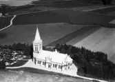 Flygbild (AB Flygtrafik) över Ölmevalla kyrka och kyrkogård med omgivande odlingslandskap.