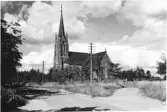 Exteriörbild av Årstad kyrka med en grusväg som delar sig i förgrunden. Förlag: Th. Persson, Årstad