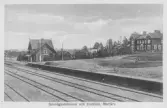 Järnvägsstation med perrong och spårområde. Intilliggande hotellbyggnad och övrig bebyggelse. Bildtext: ”Järnvägsstationen och Hotellet, Morjärv.”