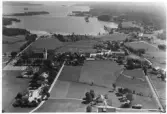 Flygfoto över Södra Unnaryd med kyrka och kyrkogård till vänster och sjön Unnen upptill i bild. Vy över bybebyggelse och odlingslandskap.