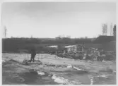 Dammen byggs 1897- En man tar sig över älven på en liten flotte.