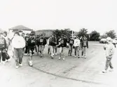 Loppmarknad på Frejaplan i Mölndal, år 1994. Spelare i fotbollslaget Jitex BK går över fotbollsplanen. Fässbergsgymnasiet i bakgrunden.