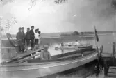 Barn på brygga ser på kajakpaddlare, 1912