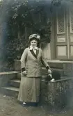 Operasångerskan Christina Nilsson i promenaddräkt och hatt tillsammans med en hund, utanför huvudingången till Villa Wik (?).