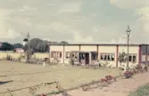 Annexbyggnad till restaurang Möllan i Morup med gräsmatta, rosenrabatt och nyplanterade träd. I bakgrunden ses tornet på Morups kyrka. 1944 köptes väderkvarnen på platsen av Hugo Eklund och Svea Augustsson, som gjorde om den till ett konditori och serveringsställe. Med tiden kom flera byggnader att uppföras vid kvarnen i takt med att verksamheten utvecklades. De drev rörelsen fram till 1960.