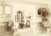 Rumsinteriör. Sannolikt från Galoschbolagets hus i Gävle, sent 1800-tal. Fotografierna uppe till höger i bild föreställer Josefina Albertina Mattsson f. Larsson samt Hans Anders Mattsson (enligt text till bilderna i album).