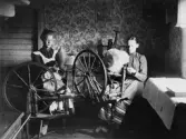 Två kvinnor vid var sin spinnrock inomhus, Hudene socken i Västergötland.