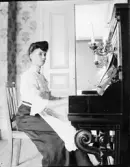 Ung kvinna sitter vid piano, Uppland