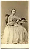 Porträtt på en kvinna i helfigur, sittande.