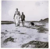 En kvinna, pojke och hund som tar en promenad på stranden. Text baksida kort: 