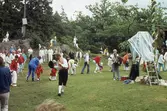 Barn och vuxna dansar kring stången vid midsommarfirande på Ekensås cirka 1982. Sångare/ledare är Sven Olof 