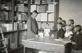 Kungsladugårdsskolan uppfördes under åren 1930-1932 och arkitekt var Ragnar Ossian Swensson.
Vaktmästare Lindqvist säljer skolmaterial i Kungsladugårdsskolan.